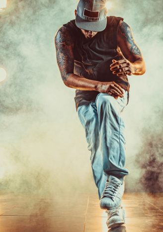 Young cool man break dancing in club with lights and smoke. Tattoo on body.
